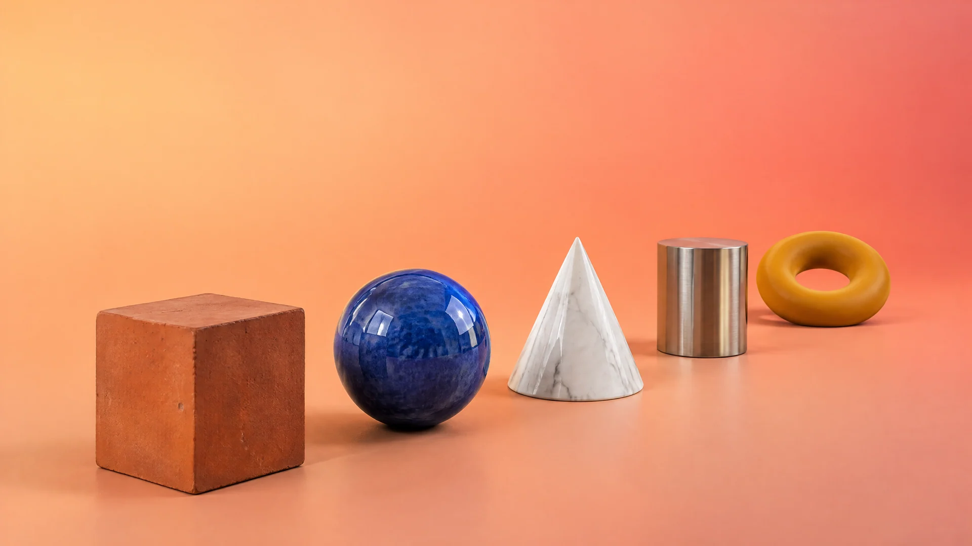 A row of a terracotta cube, blue ceramic sphere, marble cone, steel cylinder and mustard rubber ring on a peach to coral gradient