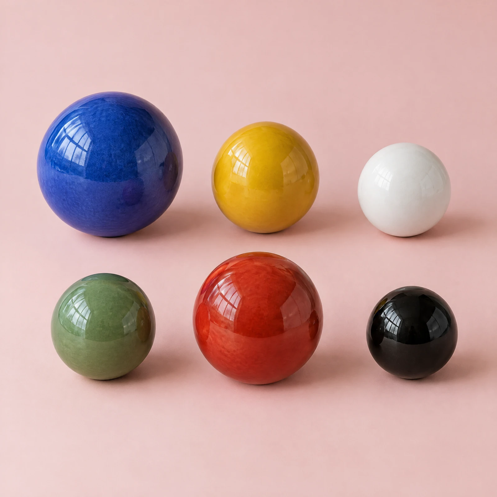 Glossy glazed ceramic spheres in blue, yellow, white, green, red and black on a blush pink background